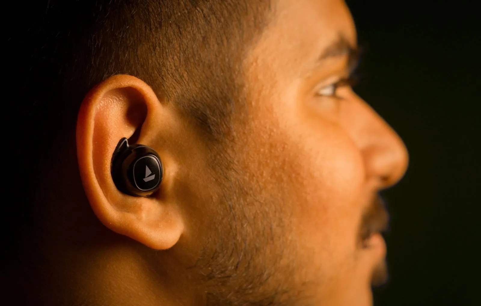 Profile view of a man wearing a wireless earbud, focusing on audio technology.